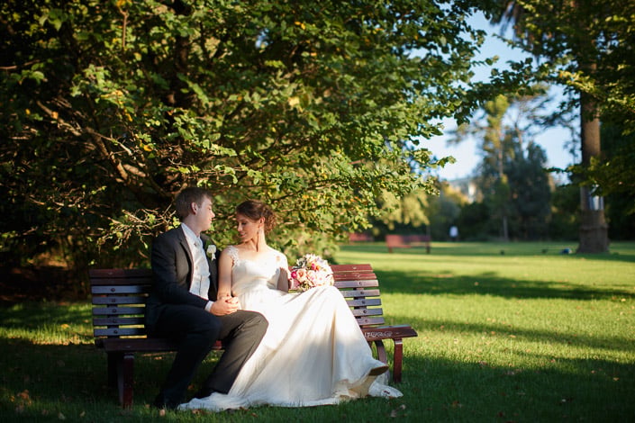 Frances and Tim sit hand in hand on a park bench in Melbourne's Royal Botanic Gardens.