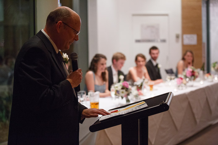 A guest delivers a speech from the lectern while the bridal table looks on.