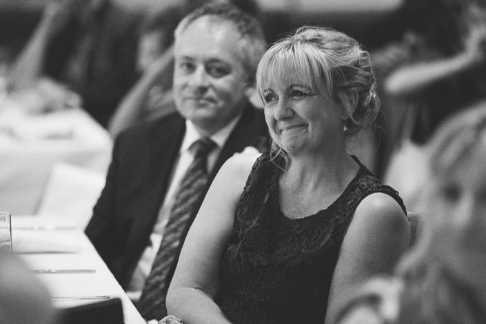 Black and white photo of a guest smiling warmly while listening to the reception speeches.