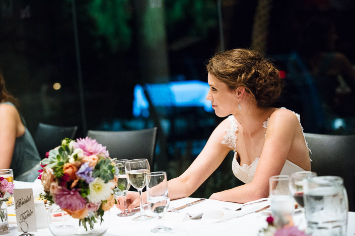 Quiet at the bridal table, Frances sits beside a tall arrangement of dahlias and succulents.