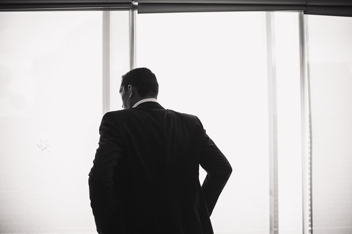 A dark-suited silhouette against the bright hotel blinds