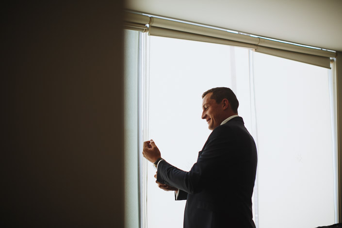 The groom grins down at his cuff by the window