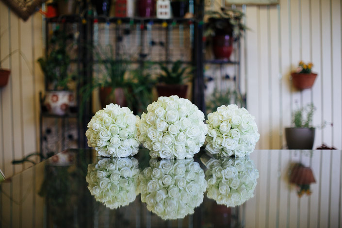 Three white rose pomanders line up on the reflective tabletop