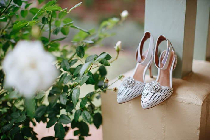 Jewel-buckled heels wait on the rendered ledge beside the rose bush