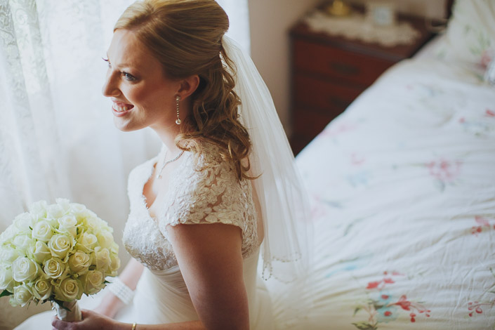 Seated at the floral bedspread, drop earrings catching the light
