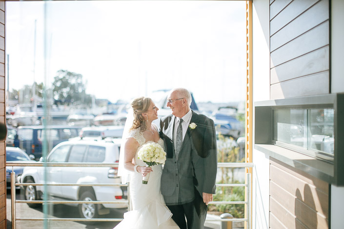 A grey haired man in glasses meets the bride at the clubhouse door above the marina.