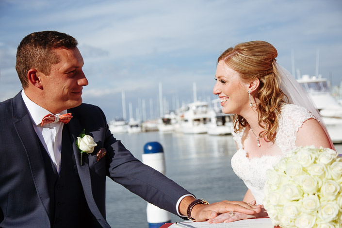 The groom's hand rests on the bride's at the signing rail, orange bow tie bright.