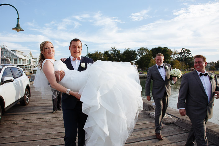 The groom scoops the bride clean off the pier as the groomsmen catch up.