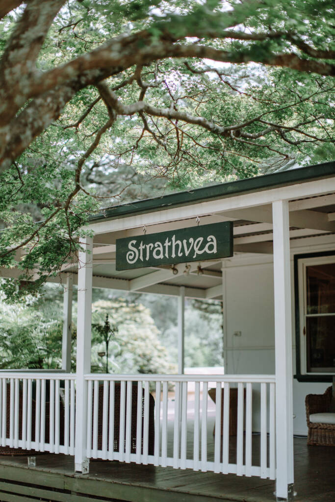 The Strathvea Guesthouse sign hangs beneath leafy branches beside the white verandah in the Yarra Valley.
