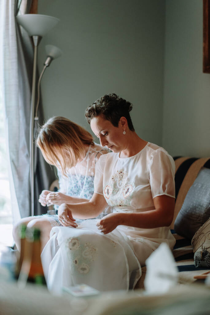 Sarah and a helper work with thread above her embroidered gown during preparation.