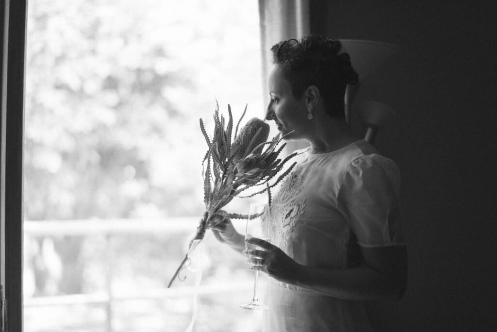 Black-and-white portrait of Sarah with her banksia bouquet and a flute beside the window at Strathvea Guesthouse.