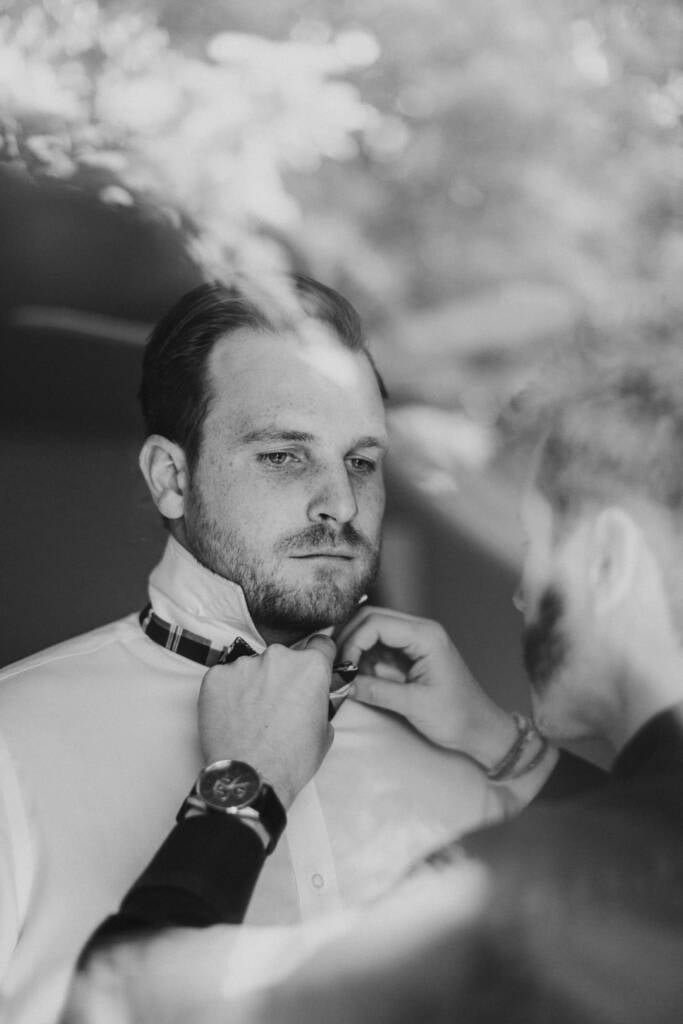 Black-and-white photo of a helper adjusting Jye's checked bow tie.
