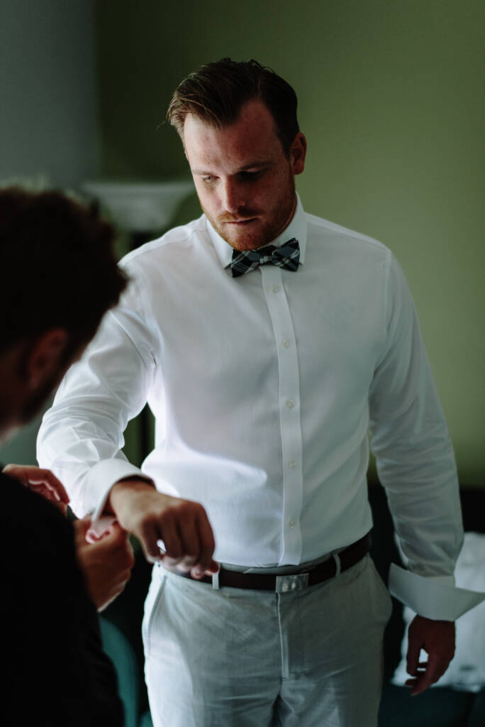 Jye looks down as a helper fastens his shirt cuff.