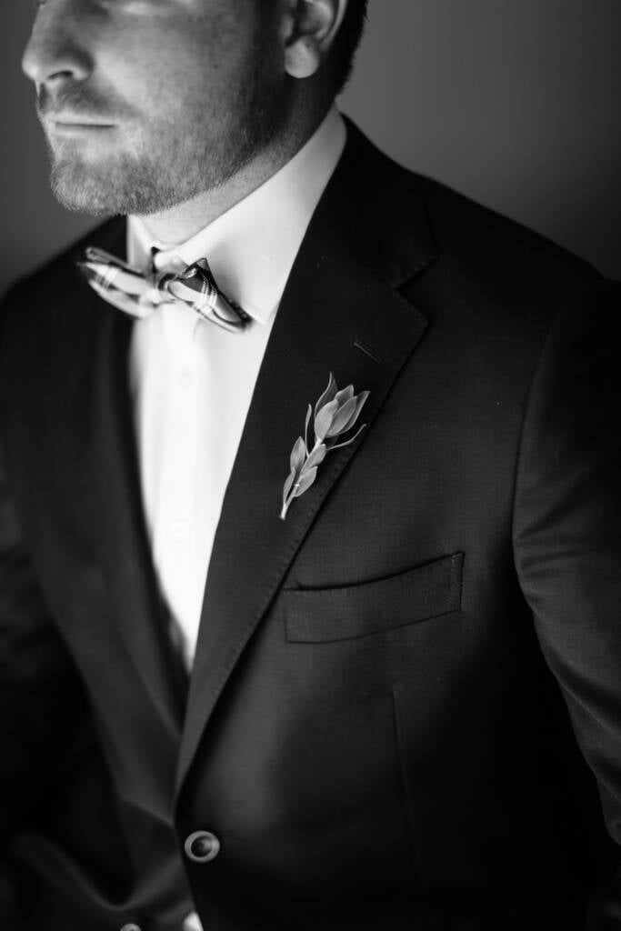 Black-and-white detail of Jye's checked bow tie and foliage boutonniere on his dark jacket.