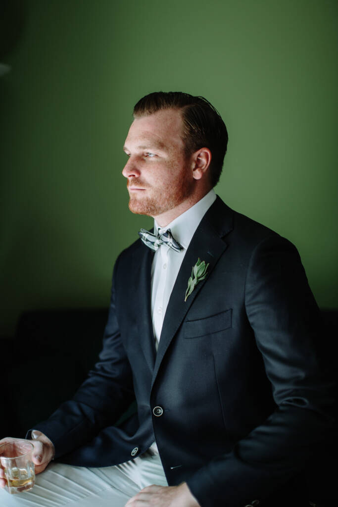 Jye sits holding a tumbler during groom preparation.