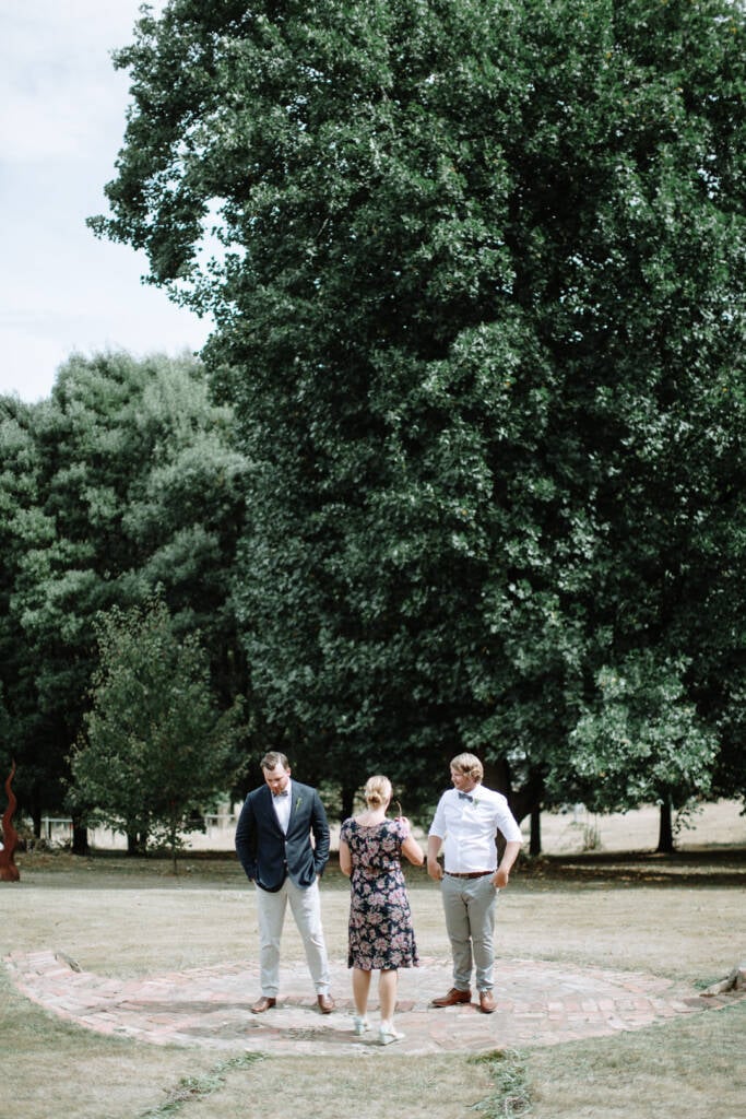 Jye stands with a companion and the celebrant on the paving before his garden wedding at Strathvea Guesthouse.
