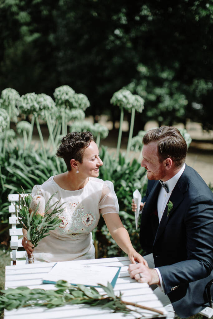 Sarah and Jye sit together at the signing table in the garden at Strathvea.