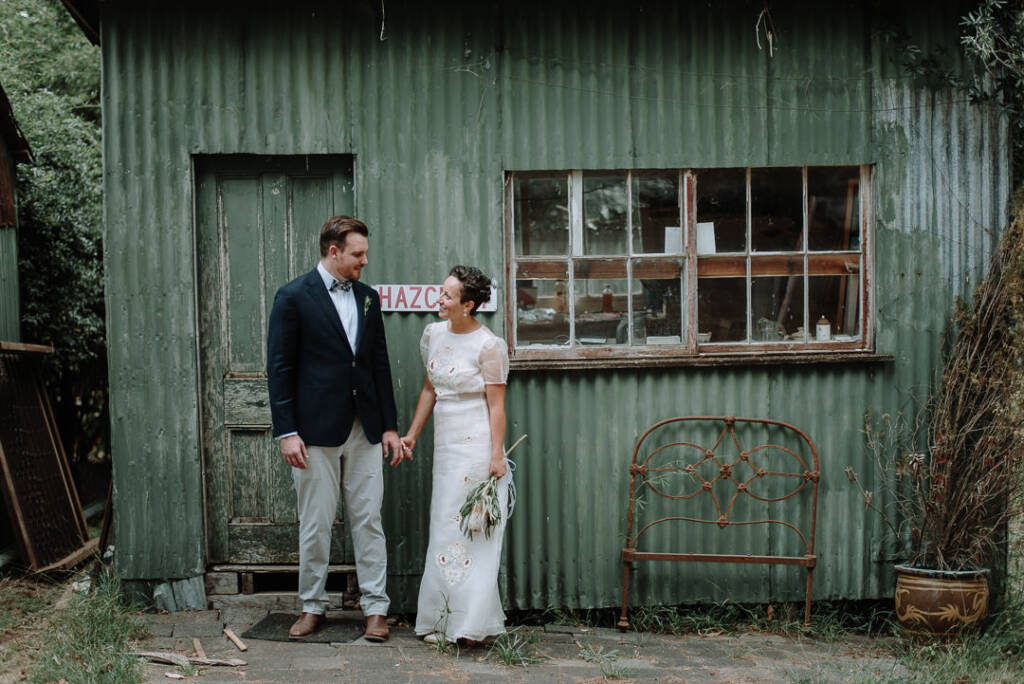 Sarah and Jye pose beside a green corrugated shed and old bedhead at Strathvea.