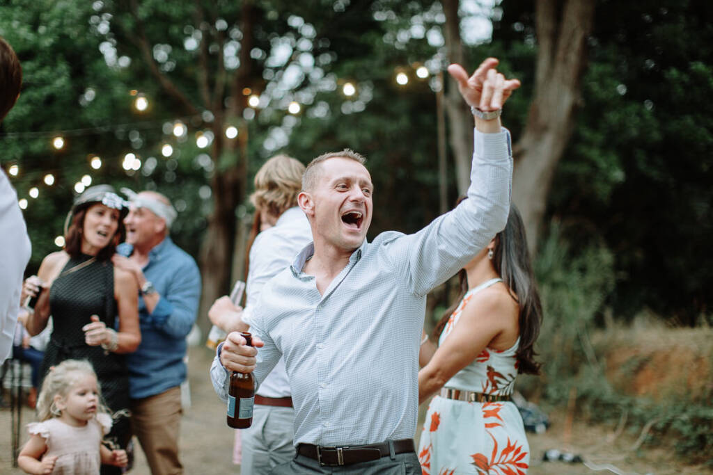 A guest raises an arm while dancing with a drink bottle beneath festoon lights at Strathvea.