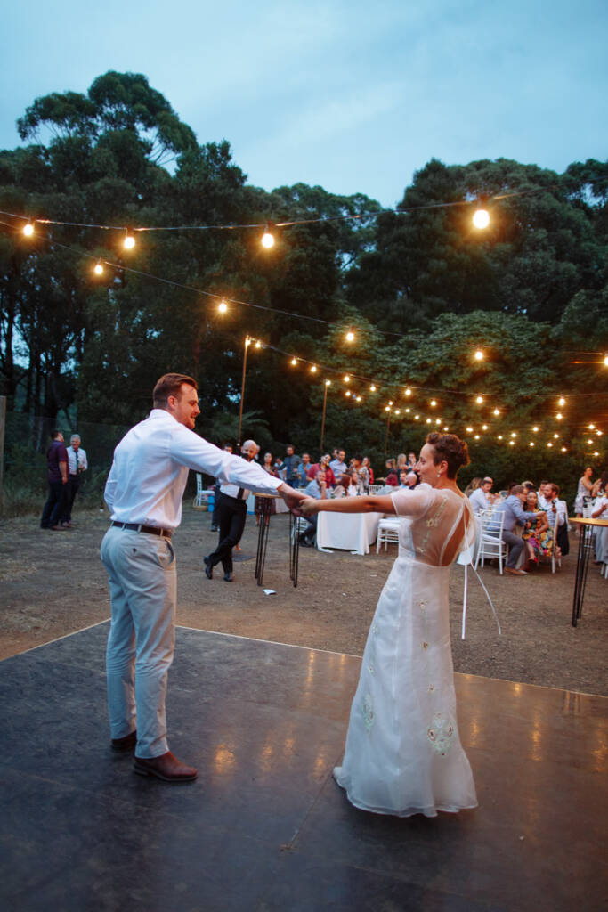 Sarah and Jye extend their joined hands across the outdoor dance floor at Strathvea Guesthouse at dusk.
