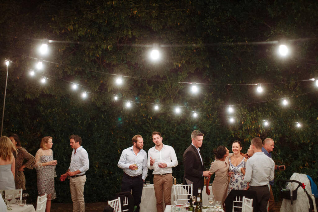 Guests mingle beside the dining tables beneath night-time festoon lights at Strathvea.