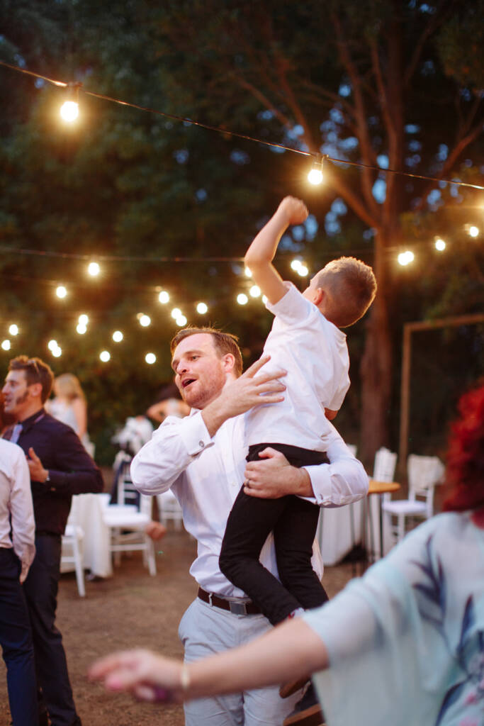 Jye lifts a child who raises an arm beneath the festoon lights at Strathvea.