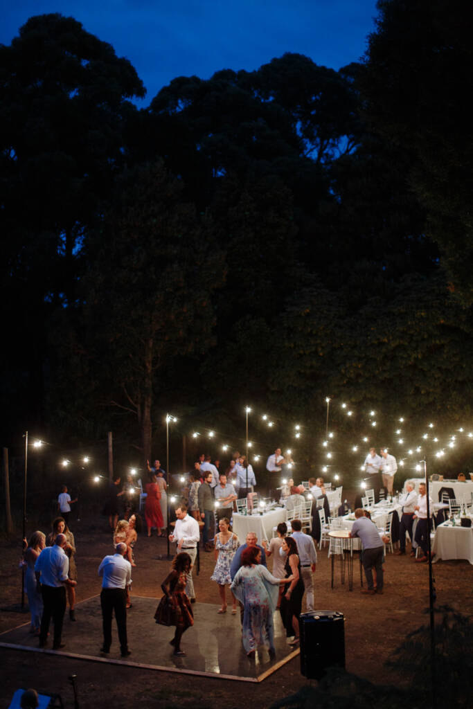 Guests dance beneath festoon lights at Strathvea Guesthouse, with the Yarra Valley treetops against a deep blue sky.