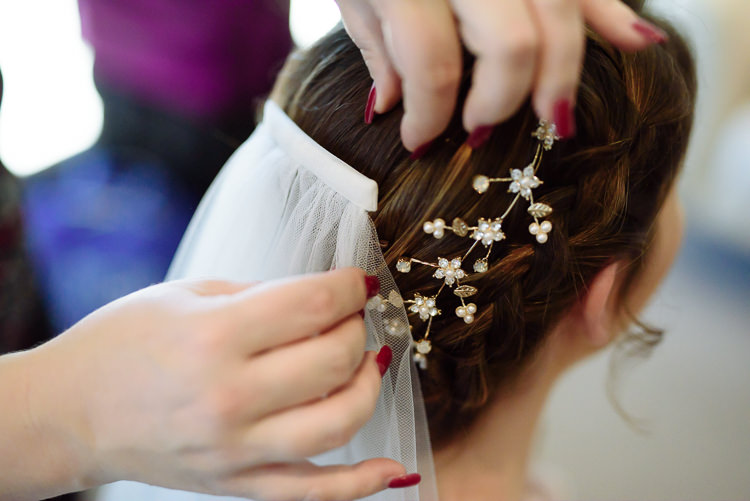 Hands with red nails fix a veil comb and a gold pearl hair vine into a braided updo.