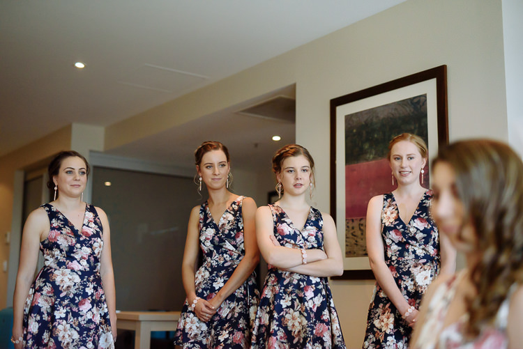 Four bridesmaids in matching floral dresses watch the bridal preparations.