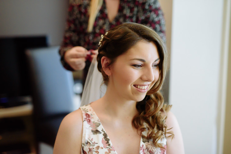 Shannon smiles in her floral dress and hair vine as her veil is pinned from behind.