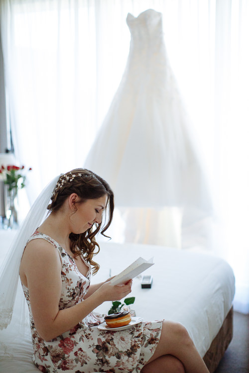 Shannon in her floral dress and veil reads a card on the bed, the gown backlit behind her.