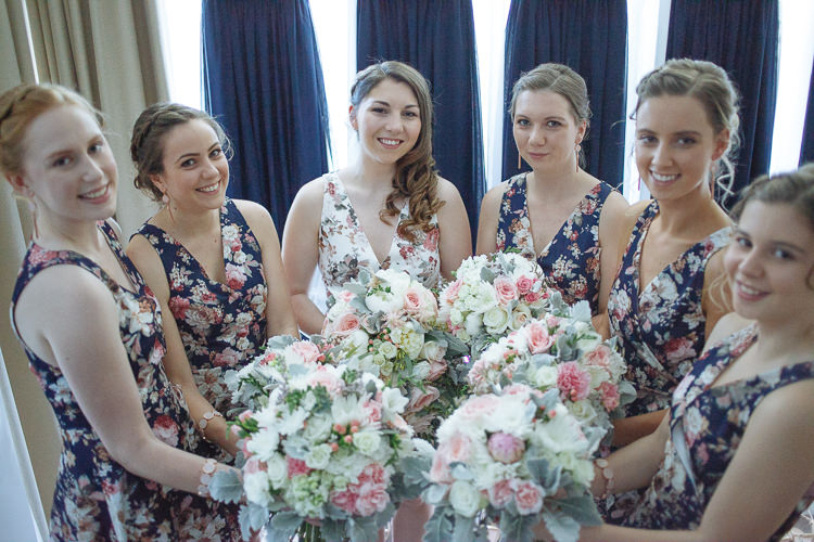 Shannon in her floral dress among five bridesmaids in navy florals, all holding blush and white bouquets.