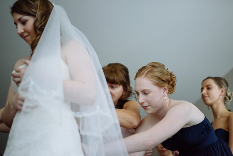 Two women help with the back of Shannon's gown beneath her veil.