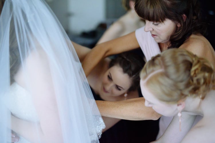 Three women concentrate on the back of Shannon's gown beneath her veil.