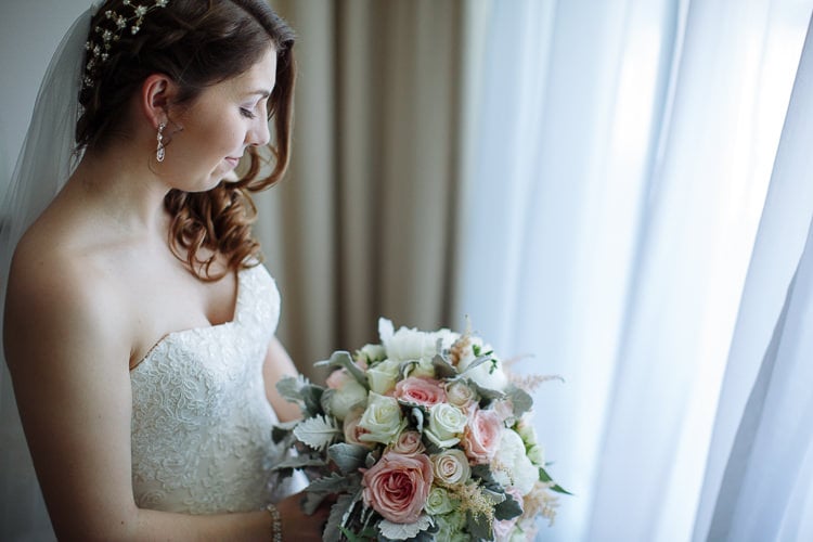 Shannon looks down at her pink and white rose bouquet beside a window.