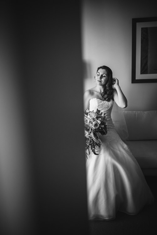 Black and white past a door edge of Shannon touching her hair on a sofa with her bouquet.