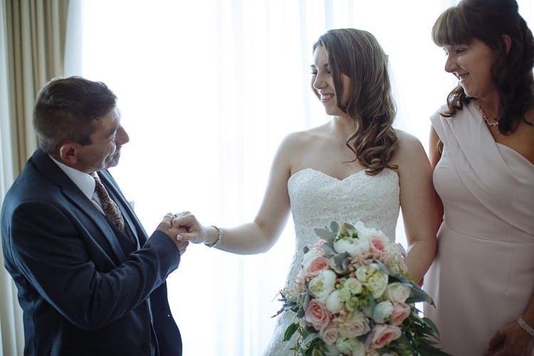 Backlit by the curtains, Shannon holds hands with a man in a dark suit, a woman beside.