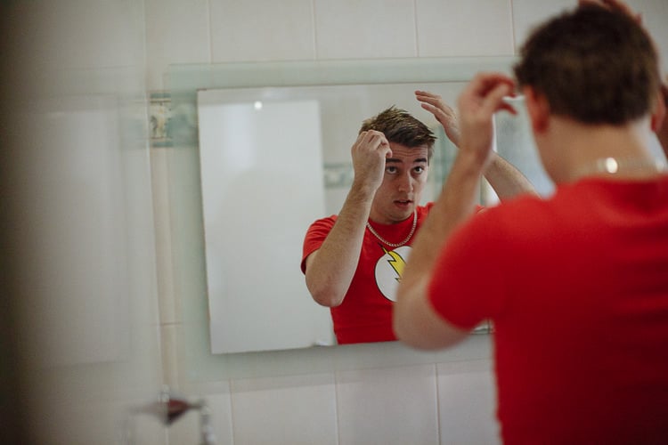 Luke in a red lightning bolt tee fixes his hair in a bathroom mirror.