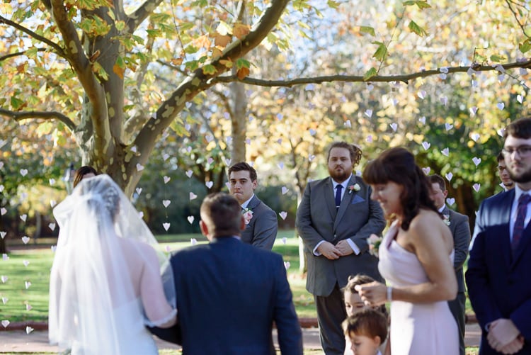 Over Shannon's veiled shoulder, Luke watches her approach with groomsmen either side.