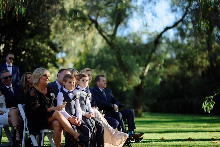 Guests and two boys in bow ties sit in white chairs on the lawn at Sunnybrae.