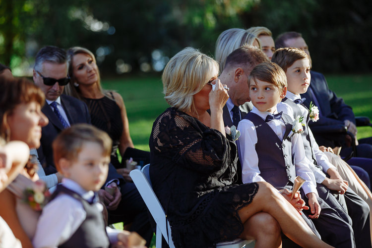 A woman in black lace wipes a tear with a tissue, a page boy on her lap.
