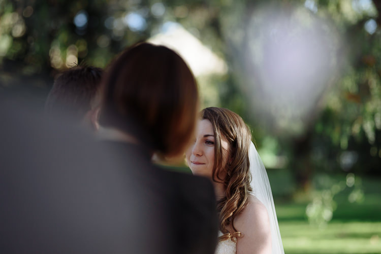 Past the celebrant's and Luke's blurred heads, Shannon in her veil looks at him with a small smile.