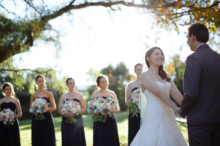 Shannon laughs while holding Luke's hands, with bridesmaids behind them.