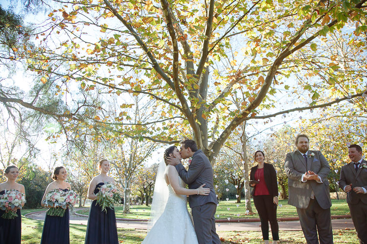 Shannon and Luke kiss beneath a leafy tree and paper hearts at Sunnybrae Estate.