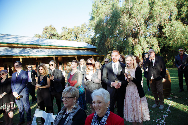 Guests applaud on the lawn at Sunnybrae, with a verandahed building behind them.