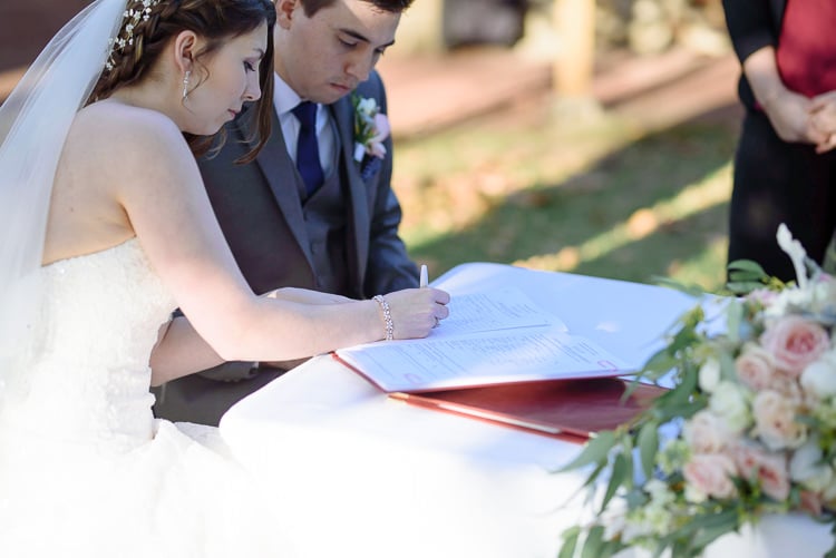 Shannon signs the register beside Luke at the flower-decorated table at Sunnybrae Estate.