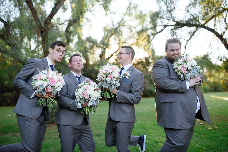 Four groomsmen pose playfully with bouquets beneath trees at Sunnybrae.