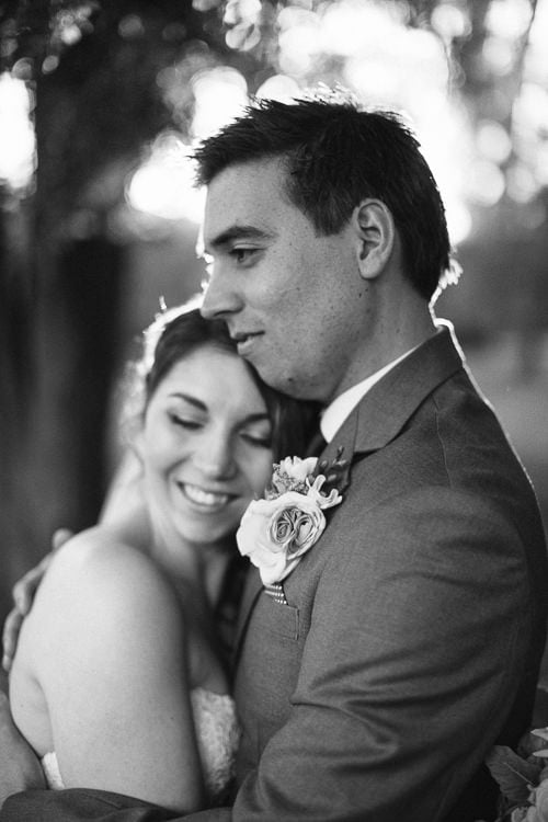 Black and white close up of Shannon smiling with eyes closed against Luke's chest, his rose boutonniere.