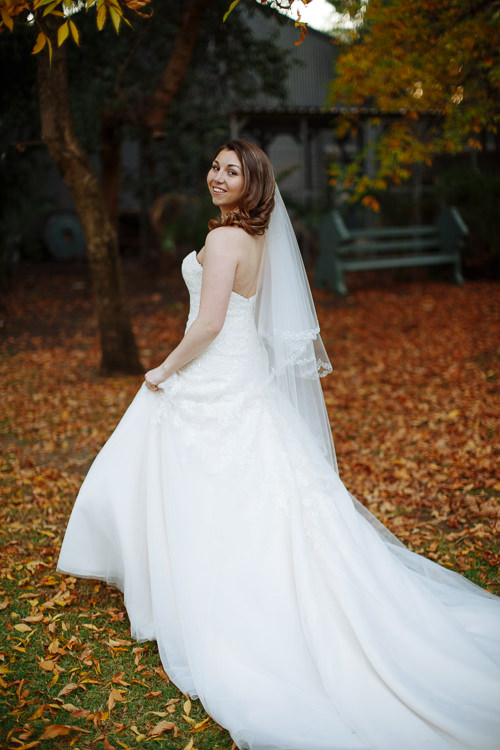 Shannon looks back smiling, her wedding dress train spread across fallen leaves at Sunnybrae Estate.