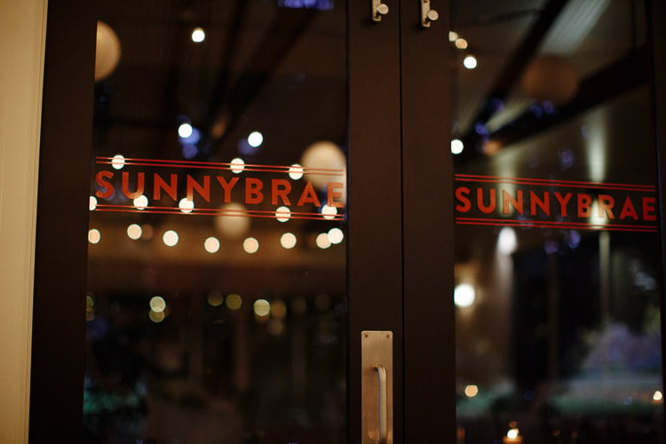 Black framed glass doors lettered Sunnybrae in red, festoon lights and paper lanterns glowing inside.